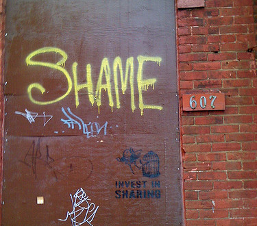 A graffiti of the word Shame on a brown wall
